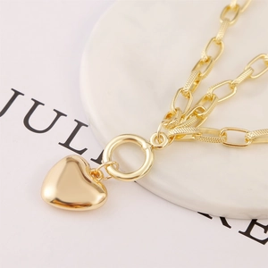 Detailed close-up of a gold heart pendant necklace with textured link chain on marble