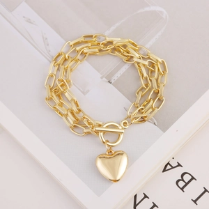 Three-layer gold chain bracelet with heart pendant and toggle clasp on a white table