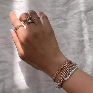 Lifestyle shot of trendy twisted croissant rings and layered gold pearl bracelets on white fabric