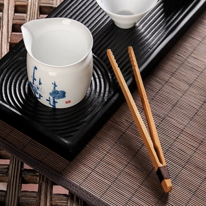 Bamboo tea tongs and white porcelain cup with blue floral pattern on a bamboo mat
