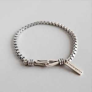 Detail eines silbernen Gliederkettenarmbands mit rechteckigem Logo-Tag und Hakenverschluss