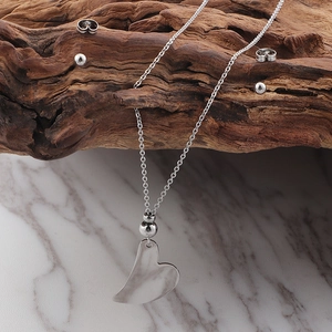 Detail of silver heart pendant necklace and ball stud earrings on natural wood and marble