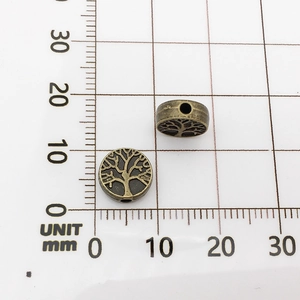 Detailed view of bronze metal tree beads on metric grid paper showing 12mm diameter size