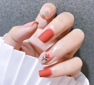 Macro shot of matte red nails with small floral patterns and glitter sequins detail