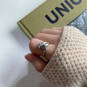 Macro detail of minimalist 925 sterling silver water drop ring on knit sweater sleeve