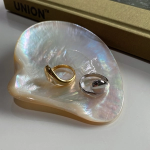 Detail view of gold and silver bean-shaped rings on a pearl tray with elegant lighting