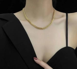 Fashionable gold stainless steel thick Cuban chain necklace worn on model against dark background