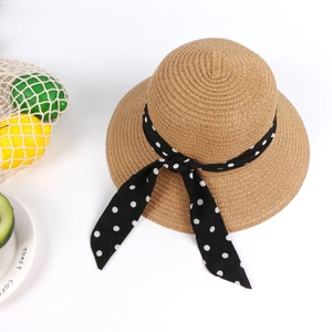 Detail of baby straw sun hat with black polka dot ribbon and woven texture on white background