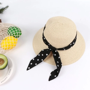 Detail of baby straw sun hat featuring a classic black polka dot ribbon and bow tie