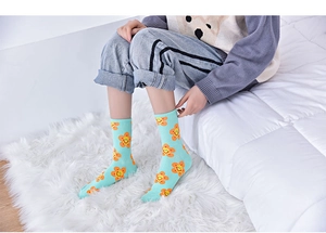 Detail of light blue crew socks with orange smiling sunflower pattern on soft white background