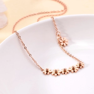 Elegant rose gold daisy necklace with five flower charms and a tassel on white ceramic
