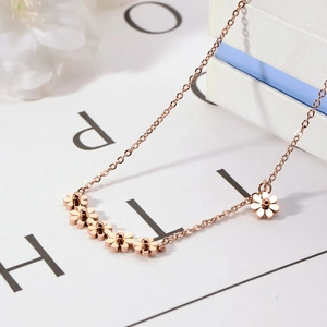 Rose gold titanium necklace with daisy flower charms on minimalist background