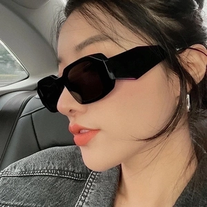 Close-up of black geometric square sunglasses worn by a model in a car setting