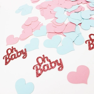 Close-up of pink heart confetti and red glittery Oh Baby cutouts on white background