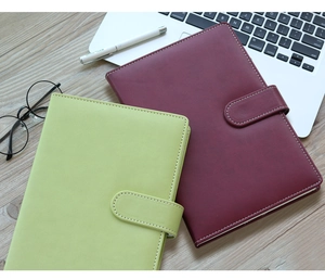 Dettaglio di taccuini in pelle verde e rosso vino con chiusura magnetica sulla scrivania
