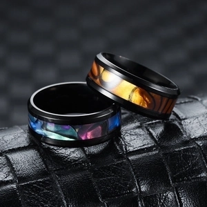 Macro shot of two men's titanium steel rings with colorful shell inlays on black leather