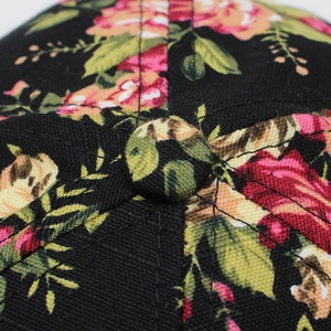 Macro view of floral rose print on crown and top button of black cotton baseball cap