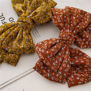 Detail of two oversized floral print bow hair clips in mustard yellow and terracotta red