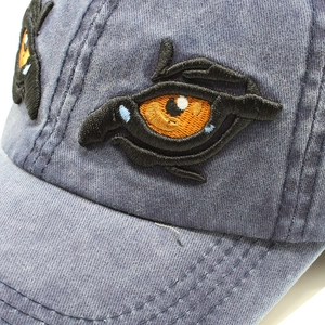 Macro shot of embroidered eye pattern and washed blue denim texture on baseball cap