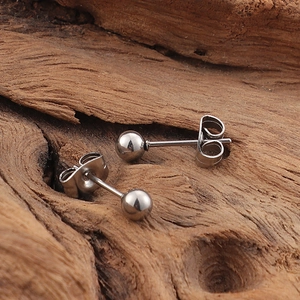Minimalist silver steel ball stud earrings pair on a natural wood textured background