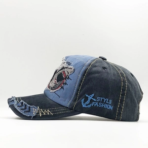 Detail of washed denim baseball cap featuring shark mouth embroidery and distressed edges