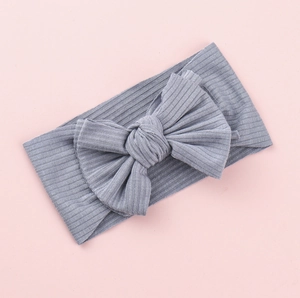 Detailed view of grey ribbed knit baby headband with a large bow on pink background
