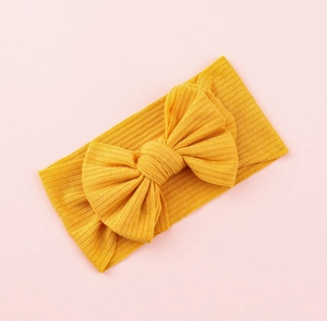 Close-up of bright yellow knitted baby headband with a large bow on a pink background