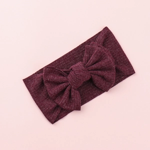 Detail of a deep burgundy knitted baby headband with a large decorative bow