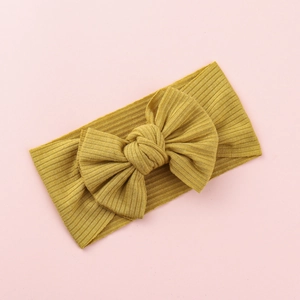 Close-up of mustard yellow ribbed fabric baby headband with large bow on pink background