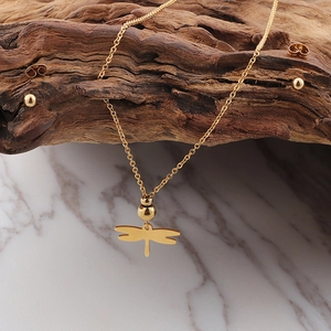 Detail of 18K gold dragonfly necklace and stud earrings on weathered wood and marble