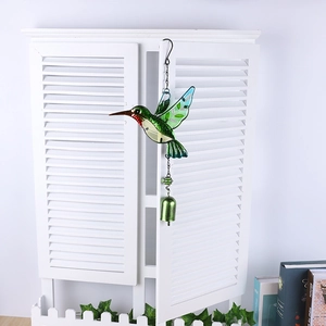 Detail of hummingbird wind chime with green glass wings and metal bell against a window