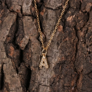 Macro detail of gold letter A pendant with sparkling crystals on natural wood background