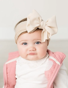 Macro detail of beige ribbed fabric baby headband featuring a large knotted bow design