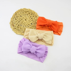 Three nylon baby headbands with large bows in orange, beige, and purple on a white base