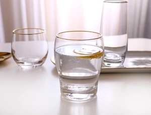 Detailed view of high and low egg-shaped glass cups with gold rims and lemon slices
