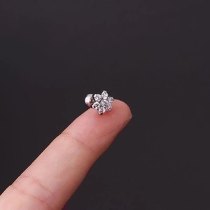 Polished stainless steel flower cartilage stud with clear crystals shown on a fingertip