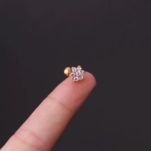 Golden flower cartilage earring with cubic zirconia crystals shown on a fingertip