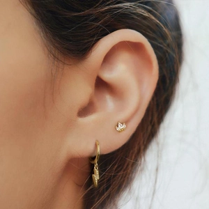Close-up of gold lightning bolt hoop and crown stud earrings worn on a model's ear