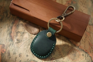 Detail of green leather AirTag holder with hand-stitched seams on vintage map background
