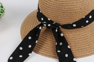 Close-up of natural straw weave sun hat featuring a classic black polka dot ribbon bow