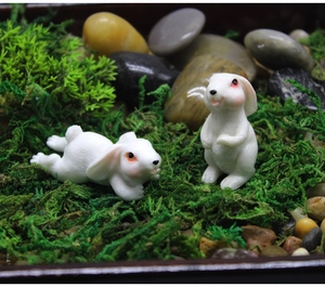 Macro detail of miniature white resin rabbits with fur textures on green moss