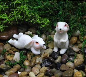 Close-up of white resin rabbits with detailed fur texture on moss and pebbles