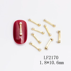 Macro detail of golden metal bar nail art studs with pearls on red manicure surface