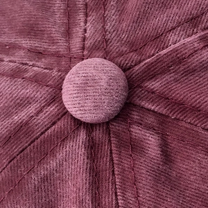 Macro shot of the top button and stitching on a burgundy corduroy cotton baseball cap