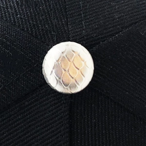 Detailed close-up of a silver-gold metallic decorative top button on black twill fabric