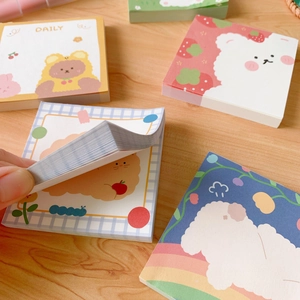 Detail view of colorful cartoon bear memo pads on a wooden desk with a hand flipping pages