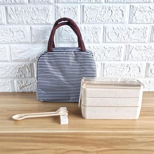 Close-up of a 3-layer wheat straw bento box with striped thermal bag and wooden cutlery