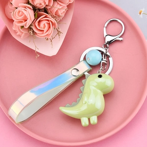 Cute green dinosaur keychain with holographic strap on a pink floral display tray