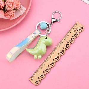 Close-up of a green dinosaur keychain with a holographic strap and a blue bead on pink decor