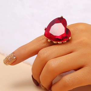 Close-up of a large heart-shaped red gemstone ring on a finger with gold plating